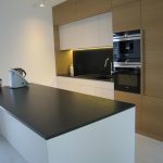 Nowoczesna kuchnia z wyspą, dębową zabudową do sufitu i białymi frontami w macie